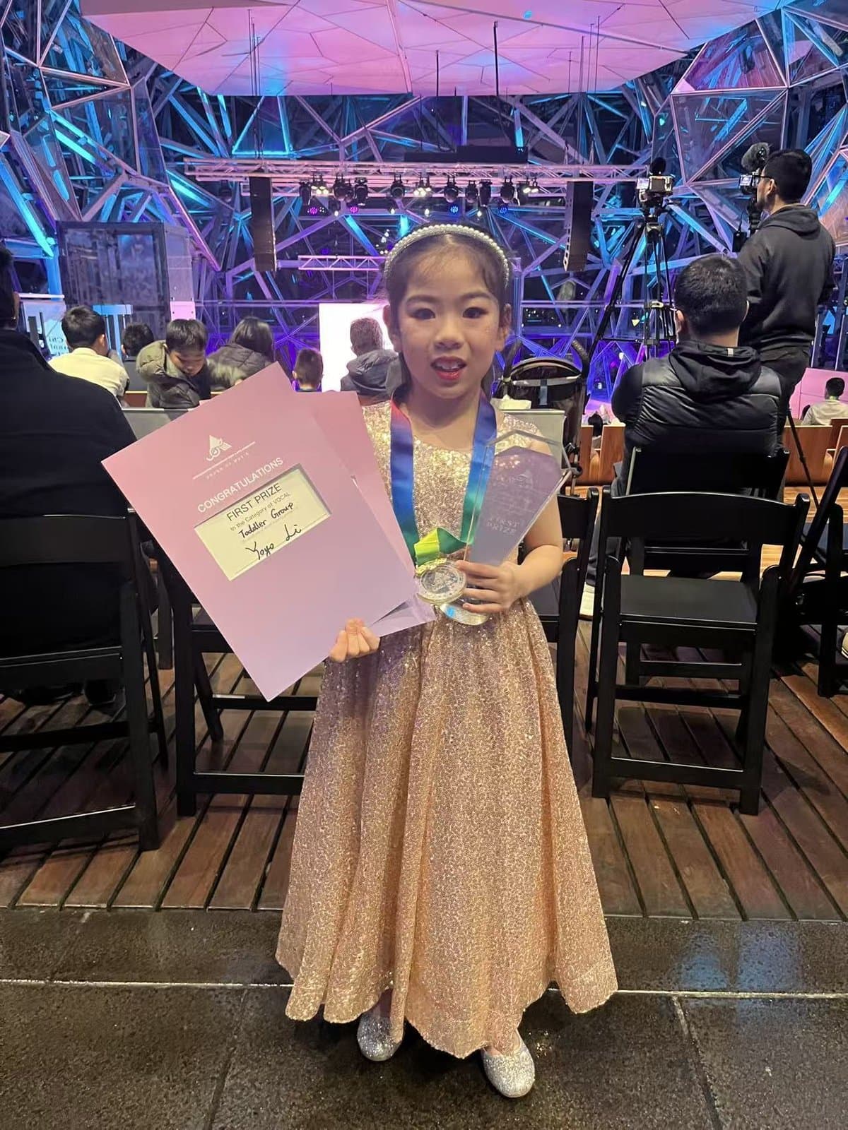 A student in a gold gown holding her certificate and medal in the foyer