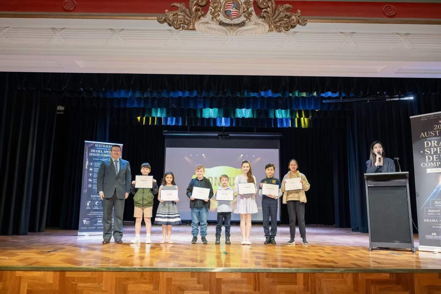 Competitors on stage at the speech and debate results with the adjudicator at the lectern