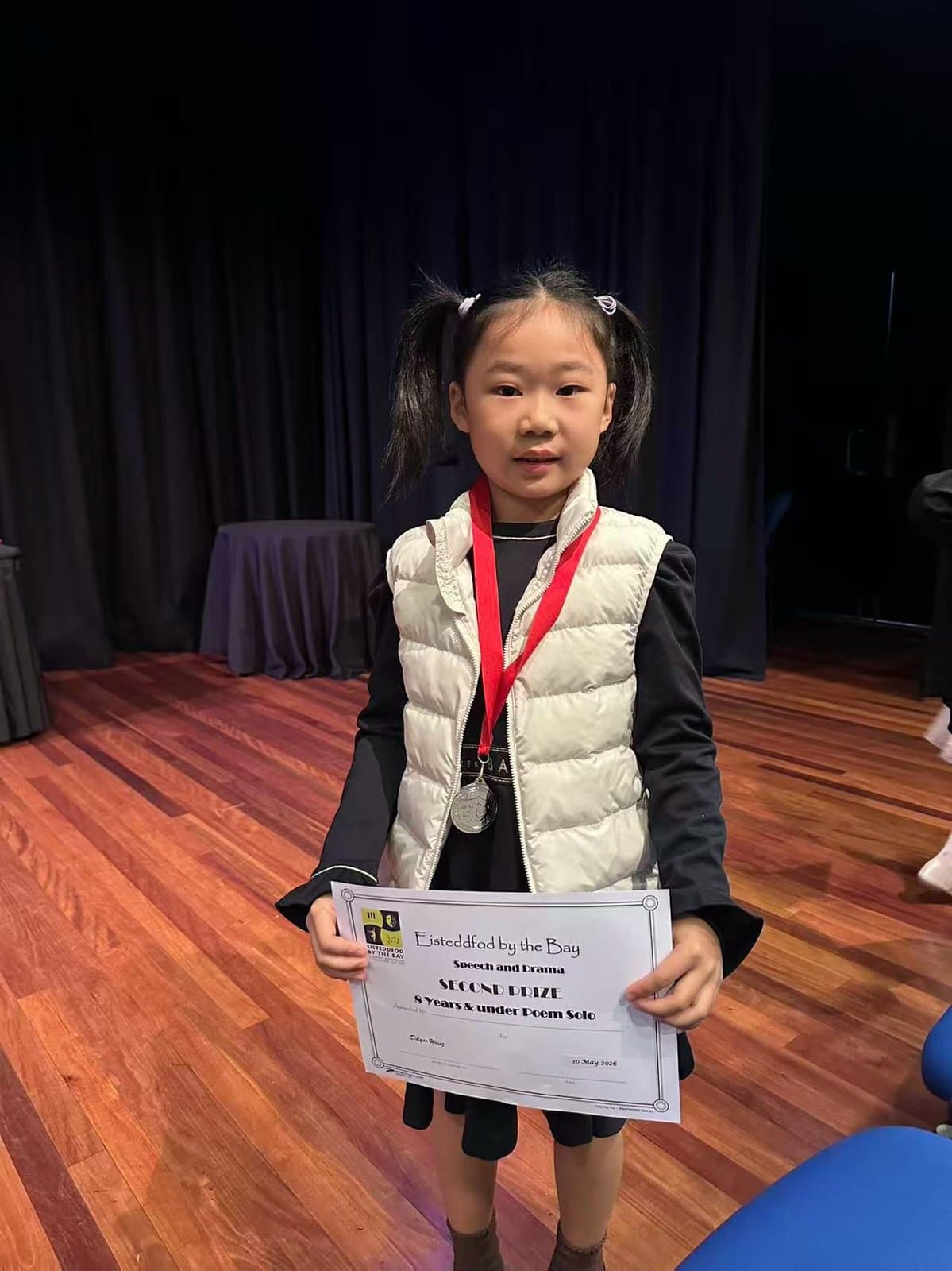 A student holding her certificate with a medal around her neck backstage