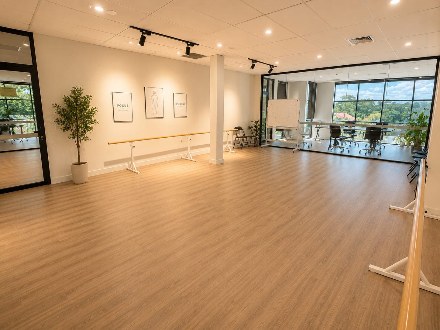 A movement studio with a ballet barre along the wall under framed FOCUS and DISCIPLINE prints, glazed through to the meeting room beyond