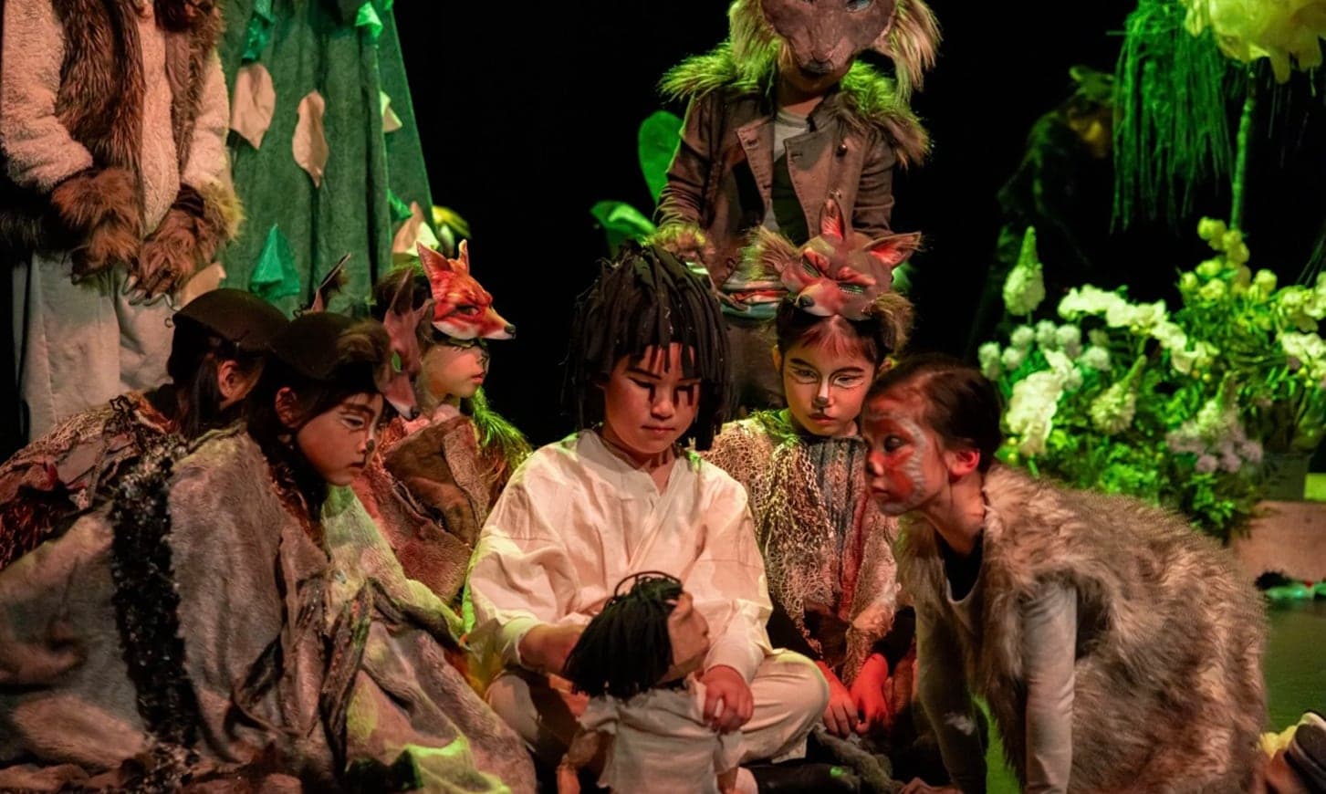 Children in animal costume and face paint, sitting close together mid-scene under green stage light in the annual production of The Jungle Book